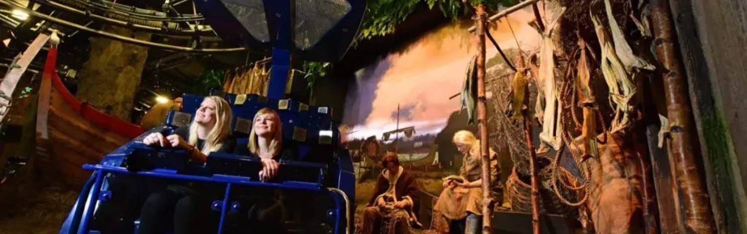 Visitors seated on a ride at Jorvik Viking Centre, moving through a Viking village exhibit with lifelike mannequins and scenery