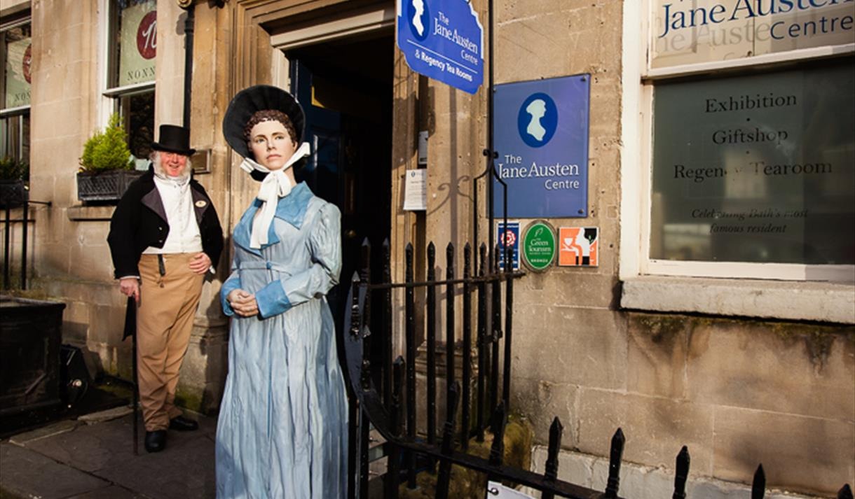 Two people stand in front of a building featuring a statue of a woman, highlighting the architectural and artistic elements