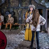 A young visitor interacts with a costumed Viking character in a detailed Norse settlement scene at the Jorvik Viking Centre