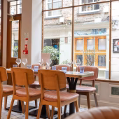 Cozy dining area with a pastel pink booth, chic tables, and a backdrop of shelves stocked with fine foods and beverages
